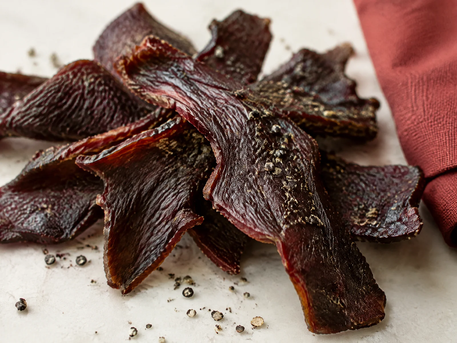 Close-up of torn beef jerky strips with cracked black pepper and a red napkin